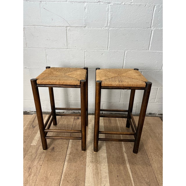 A beautifully crafted pair of Mid-Century Modern stools featuring handwoven rush seats set within richly toned walnut...