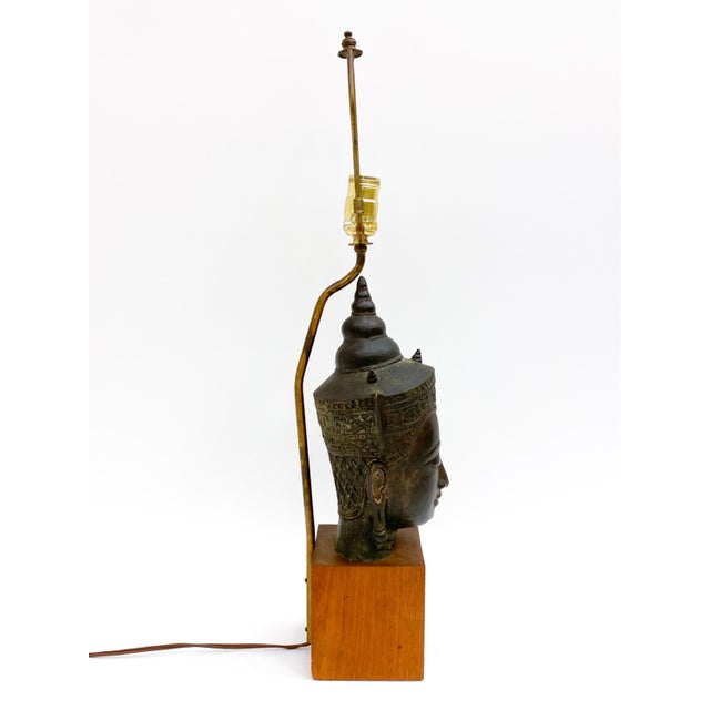 A 19th century Southeast Asian bronze Buddha head mounted as a table lamp on a square wooden block base with brass...
