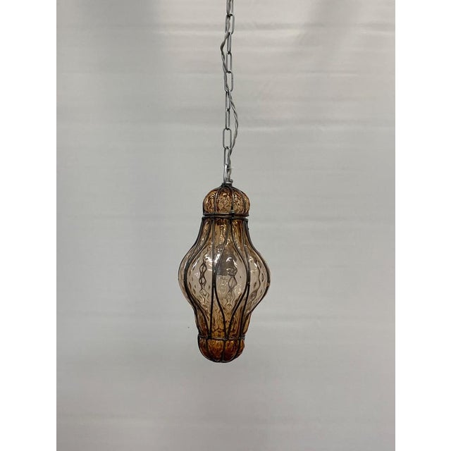 Medium-sized Murano glass hanging lantern, elegantly decorated with a curled iron-colored brass frame surrounding a finely...