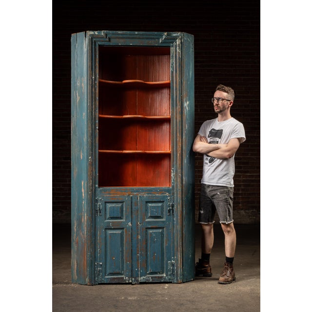 Primitive corner cupboard in worn blue paint over red wash, with true hand-cut joinery and panel doors. This cabinet is a...