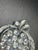 The brooch features a stylized leaf or heart outline framed by feathered, textured silver-tone leaves that curve upward...