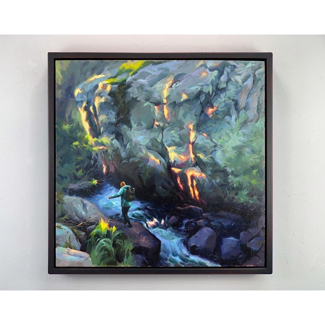 In "Transmission," a figure stands poised on the edge of a rushing stream, surrounded by lush greenery and dramatic rocky...
