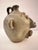 A face emerges from the body of this stoneware jug, built up in heavy relief rather than painted on. The speckled grey...