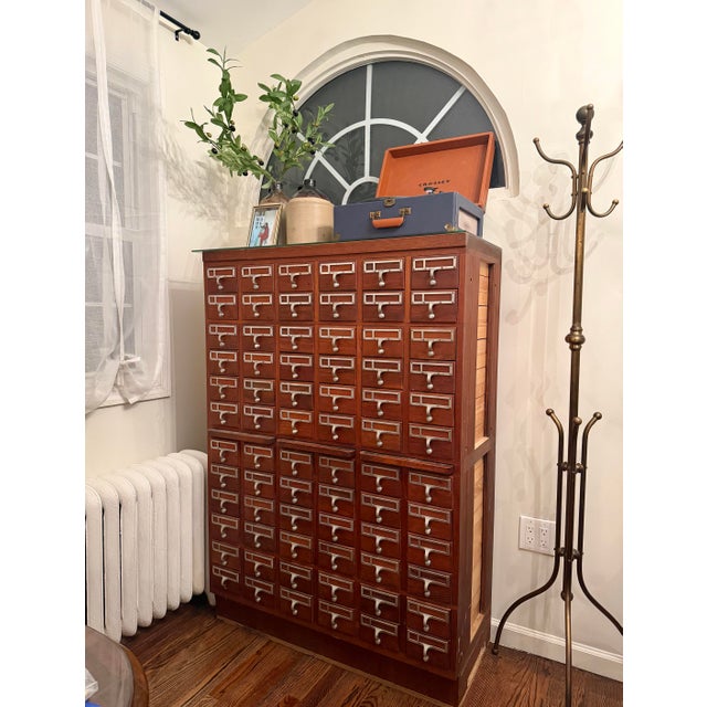 A striking vintage apothecary-style library card catalog cabinet featuring 72 individual wooden drawers, each finished...