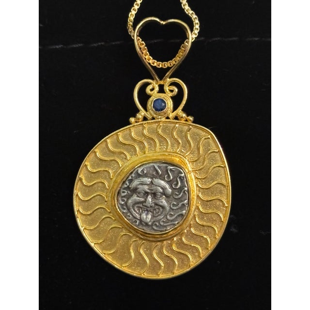An AR Drachm Gorgoneion Pendant w/ Serpents in 22 Karat gold wide surround and blue diamond accent at top. This gorgoneion...