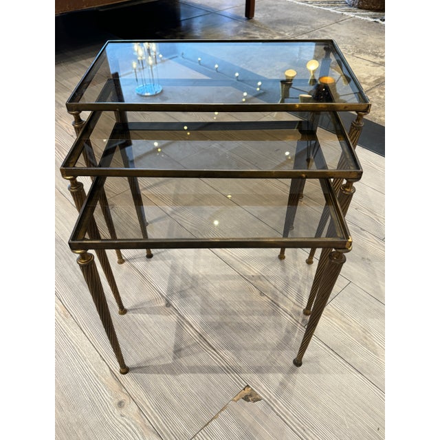 Lovely Mid-Century French Brass Nesting Tables With Smoke Glass. Features three size tables with simple decorative legs...