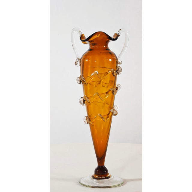 Stunning amber blown glass vase. It has a conical shape with two clear glass handles and a transparent circular base....
