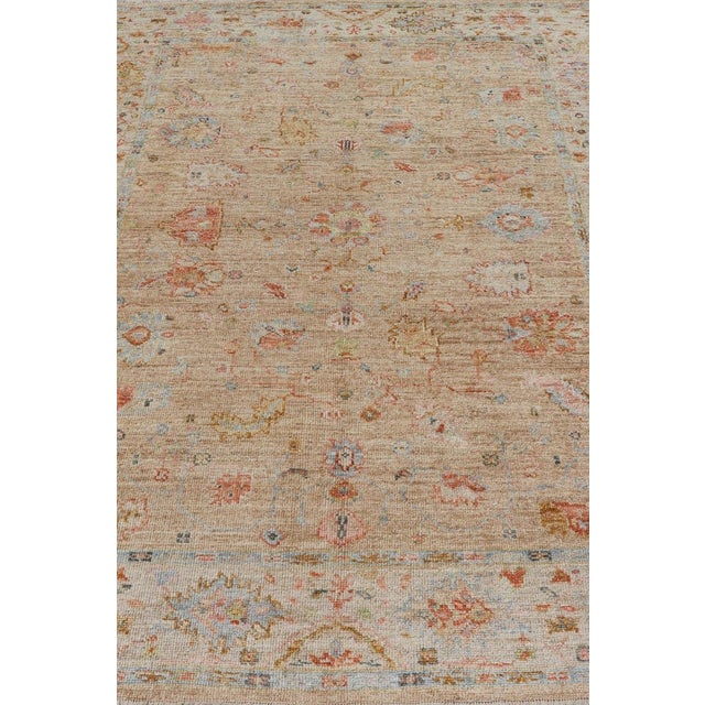 This Turkish Oushak was hand-knotted with angora wool. The field's background is rendered in a sandy-taupe, while the...