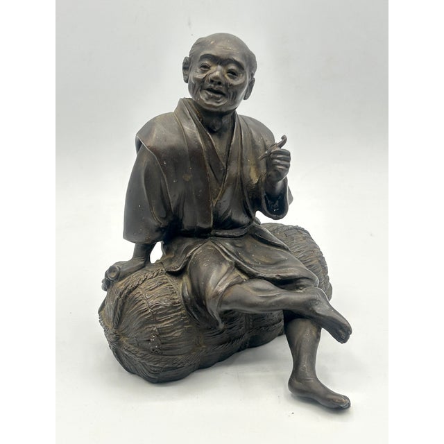 Finely modeled Japanese Meiji-period patinated bronze okimono, circa 1890–1910, depicting a seated man enjoying a...