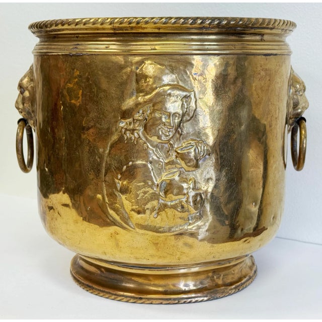 Antique hammered brass cachepot planter with a repousse depiction of a man with cup to two sides and ringed lion head...