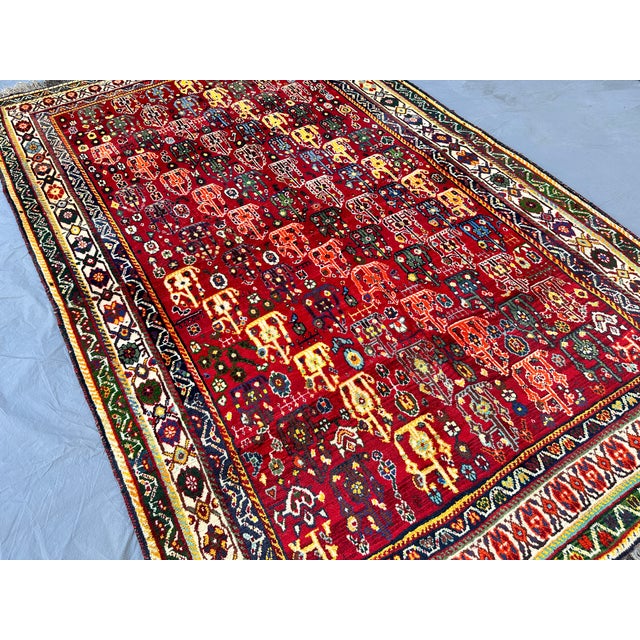 A dense, lively field of small multicolor boteh motifs fills this hand-knotted Shiraz rug, set against a deep red ground...