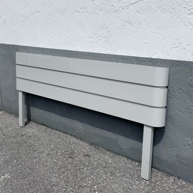 A sleek and understated postmodern king-size headboard, finished in a soft light gray gloss laminate with smooth, rounded...
