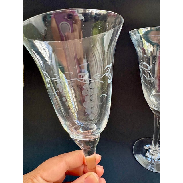 Elegant pair of vintage clear glass wine glasses featuring delicate etched grapevine decoration and graceful tulip-form...