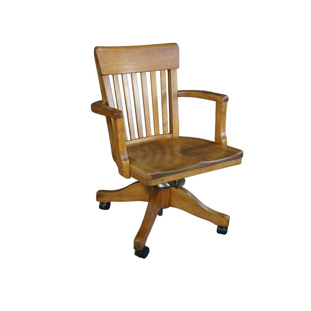A classic vintage banker's desk chair crafted from solid oak with a warm, medium honey finish, dating back to the 1920s...
