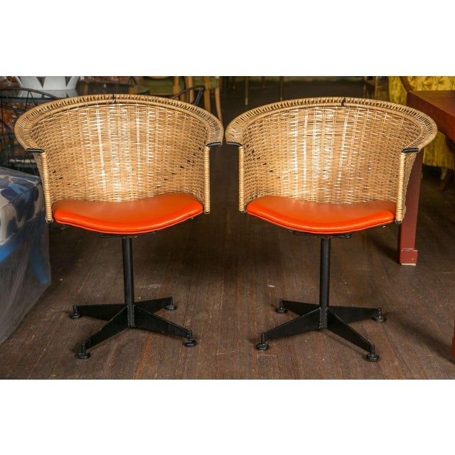 Pair of black iron swivel chairs with protectively wrapped rattan backs and orange vinyl seats. Seat height is 17.5".