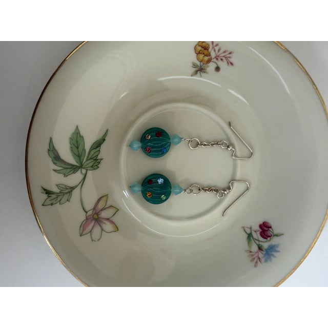 The core focal point is a ribbed, translucent green glass or resin bead shaped like a piece of hard candy. Each side of...