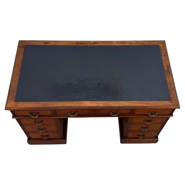 A handsome 19th-century English pedestal desk, finely crafted from walnut and distinguished by its blue leather writing...