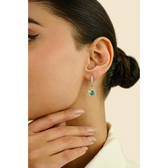 These modern huggie drop earrings feature 2 round cut emerald cut totaling 1.3 carats, set in 14K white gold. Each emerald...
