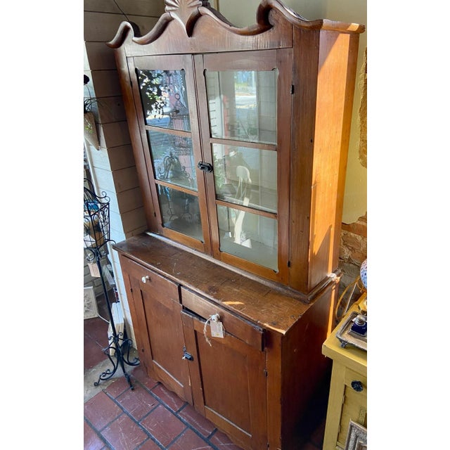 This antique farmhouse cupboard features a beautiful patina, glass fronted doors, and what appears to be original brass...