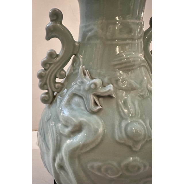 A celadon-glazed ceramic table lamp with a soft, pale green-grey finish throughout. The body is decorated with raised...