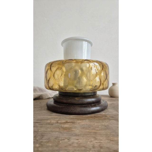 A distinctive mid-century table lamp featuring a rounded amber glass body, a frosted white glass upper element, and a...