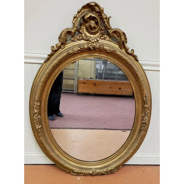 Mid-19th century American Rococo Revival oval giltwood mirror. Patina to the giltwood and some cracks commensurate with...