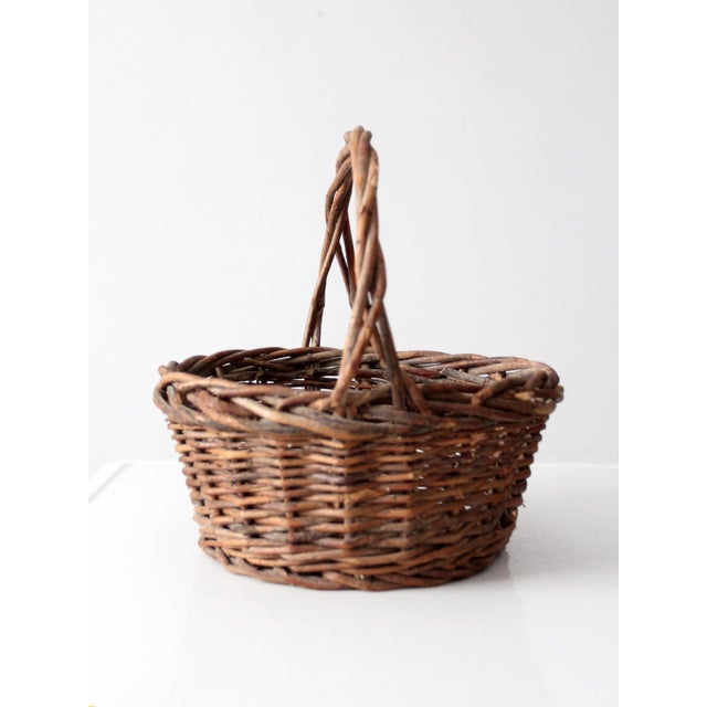 A vintage woven willow basket with a deep, rounded form, high arched handle, and wonderfully irregular twig weave. Natural...