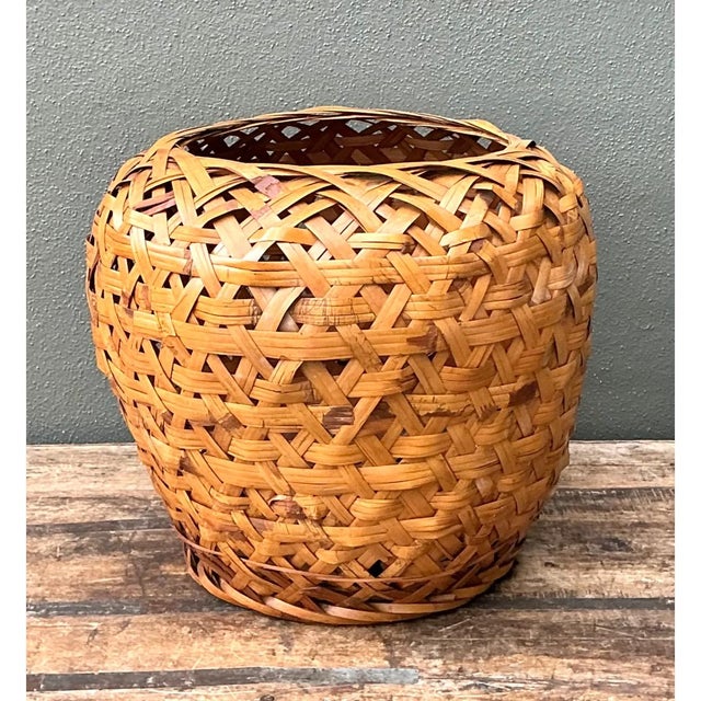 This vintage woven rattan floor basket presents a full, bulbous silhouette, with broad, rounded shoulders that taper...