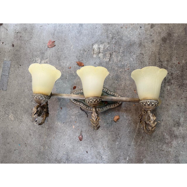 Ornate pair of three-light vanity wall sconces with a bronze-tone finish. Each fixture has three frosted yellow glass...
