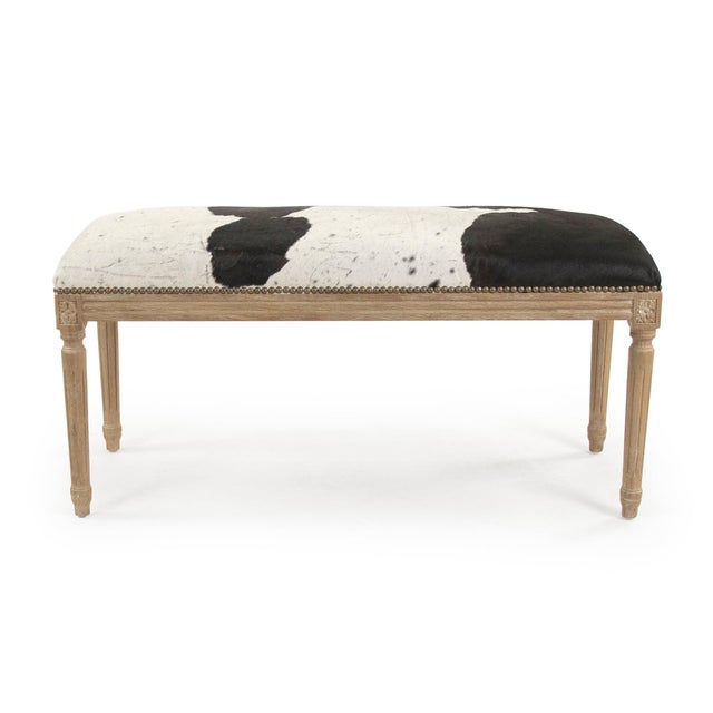 This is a bench featuring a sophisticated design with cowhide upholstery and an oak wood frame. The upholstery showcases a...