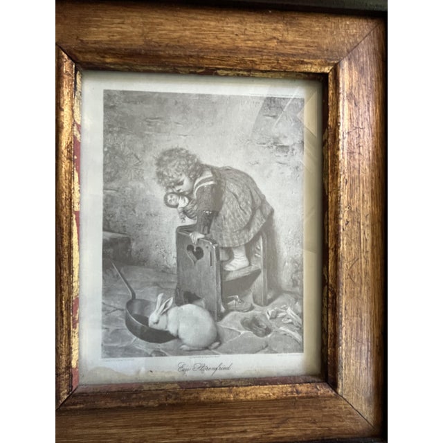 Exquisite antique framed print depicting a young girl standing on a small wooden stool while tending to a rabbit on the...