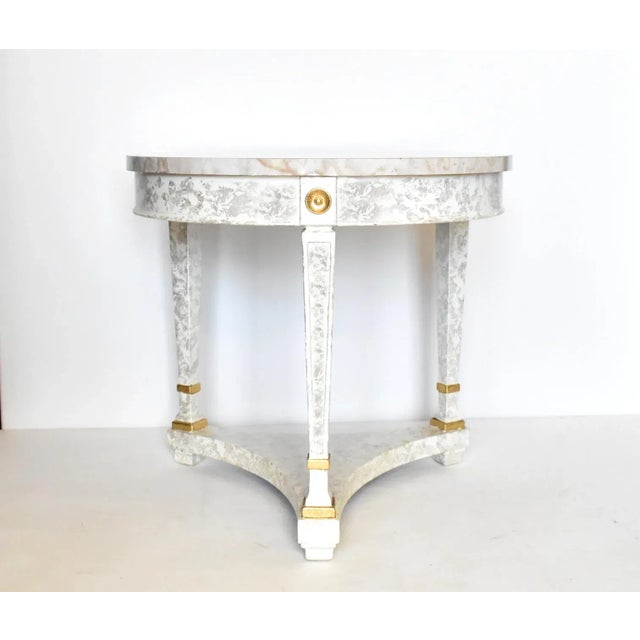 A vintage round, three-legged side table in a neoclassical style, with tapered legs, a faux marble laminate top in gray,...