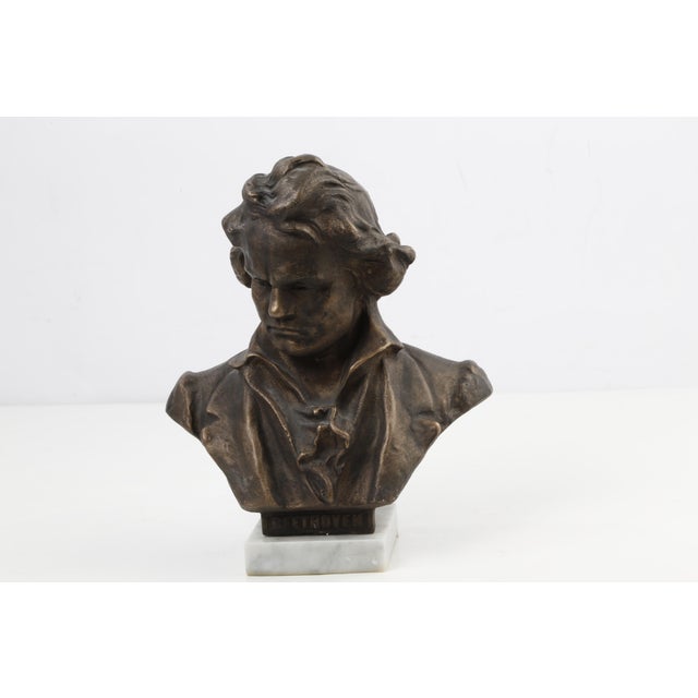 The bust is crafted with a rich bronze-toned finish and comes securely mounted on a solid, polished white/gray veined...