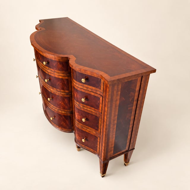 A Maitland-Smith commode in richly figured flame mahogany, its bowfront center bank flanked by two curved columns of...