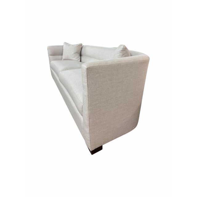 Clean-lined, low-profile sofa upholstered in a soft, textured cream performance fabric (Turbo Cream) with dark walnut...
