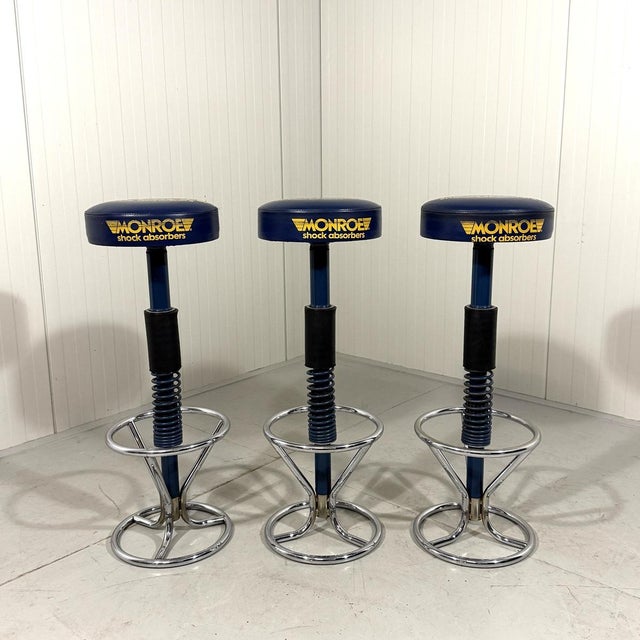 Set of 3 bar stools made in a limited edition for Monroe shock absorbers. Blue vinyl seats with yellow printing, chrome...