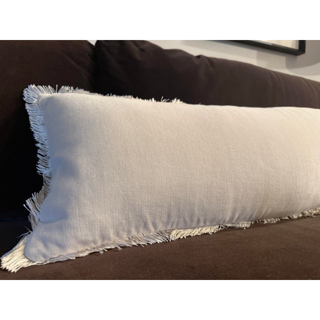 Discontinued CB2 Bettie oversized lumbar pillow in warm white velvet. The elongated silhouette features tonal fringe along...