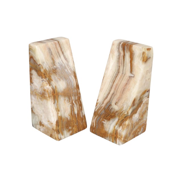 A pair of wedge shaped bookends made of onyx. Richly banded and swirling patterns in tan, caramel and cream form the...