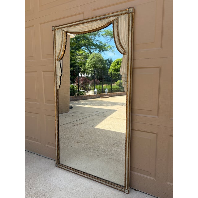 An elegant Hollywood Regency giltwood mirror featuring carved trompe l'oeil faux drapes over a mirror, in a beautifully...