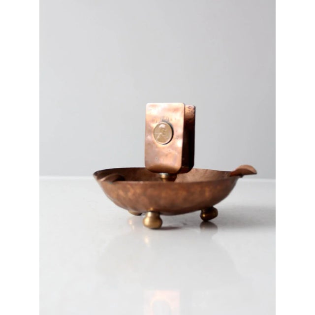 This is an antique copper ashtray with match holder. The hammered copper ashtray bowl features three pedestal feet and...