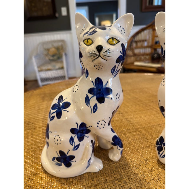 Elegant pair of Faience ceramic cats in blue and white floral pattern with yellow eyes. One of the back paws is missing -...