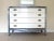 A painted white, metallic, and grey dresser and mirror. Minor wear on paint with age and use. 48” wide. 20.5” deep. 34.25”...