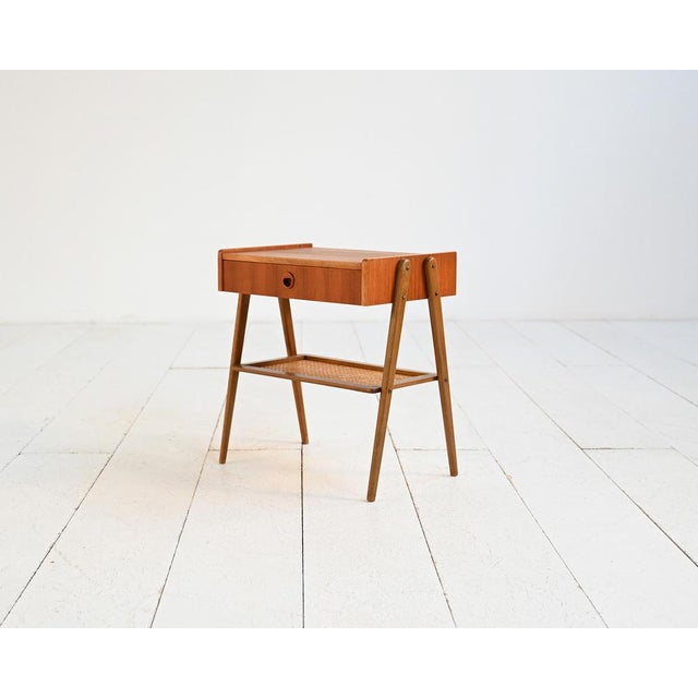 Scandinavian-made teak bedside table with a front drawer and a woven rattan lower shelf. 1950s. Light lines and slender...