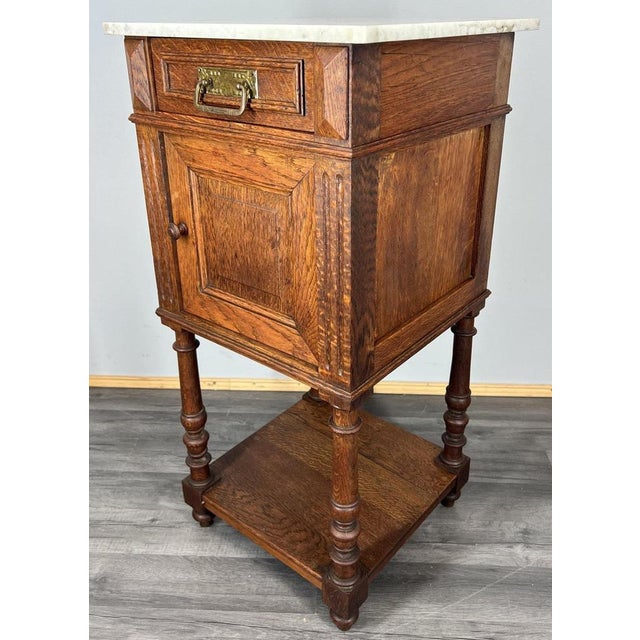 This antique French bedside table is a fine example of traditional craftsmanship and elegant materials. Featuring a white...