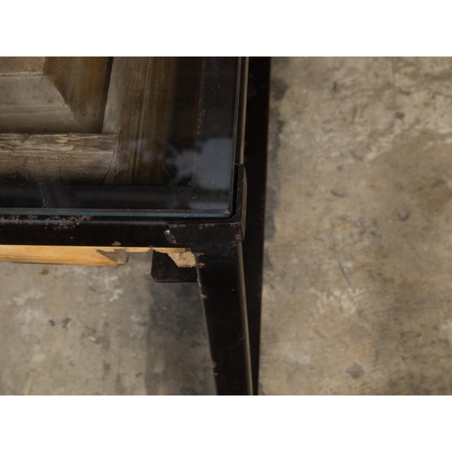 A contemporary coffee table made from an antique wooden fragment door with raised motifs under glass and mounted on a...