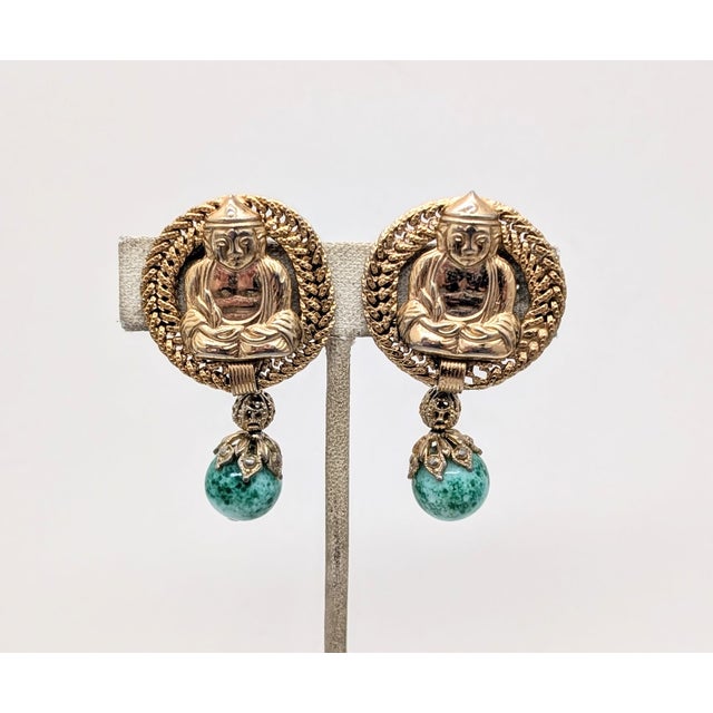 Rare 1960s goldtone round tops with a seated Buddha figure in the center with looped surround with a faux-jade drop at the...