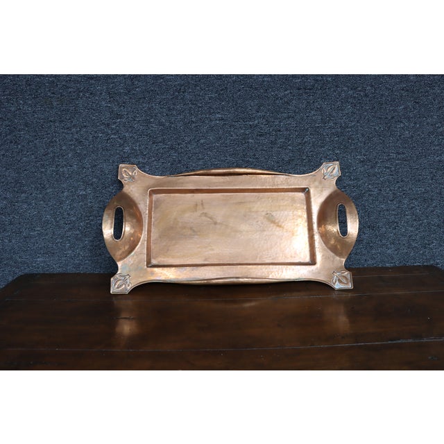 Art Nouveau copper serving tray with integrated side handles and embossed stylized leaf motifs at each corner. The tray...