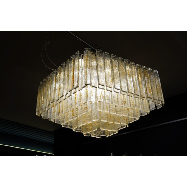 A large square pendant lamp composed of six rows of rectangular glass prisms suspended at varying heights in a cascading...