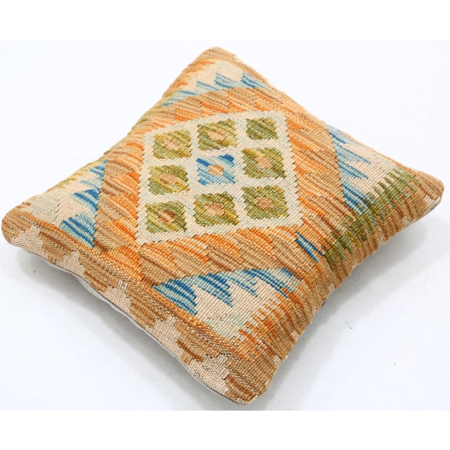 A one-of-a-kind handwoven Afghan wool kilim accent pillow featuring a central diamond medallion in gold, green, and blue....