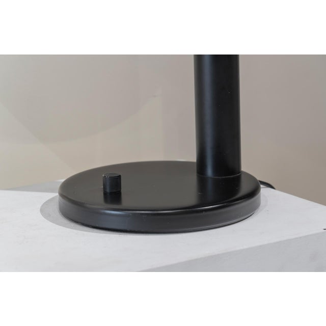 Table lamp made of black lacquered metal. Circular base with dimmer switch, tubular shaft, and circular shade housing two...